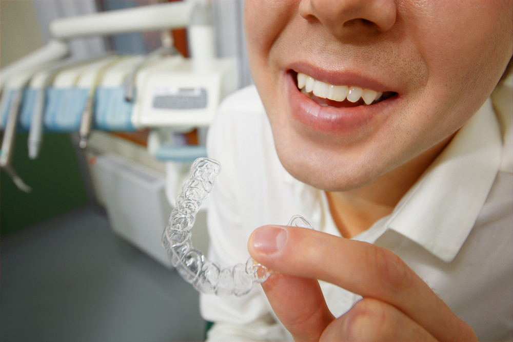 Close-up shot of man with big smile holding mouth guard or orthodontic retainers in dental office