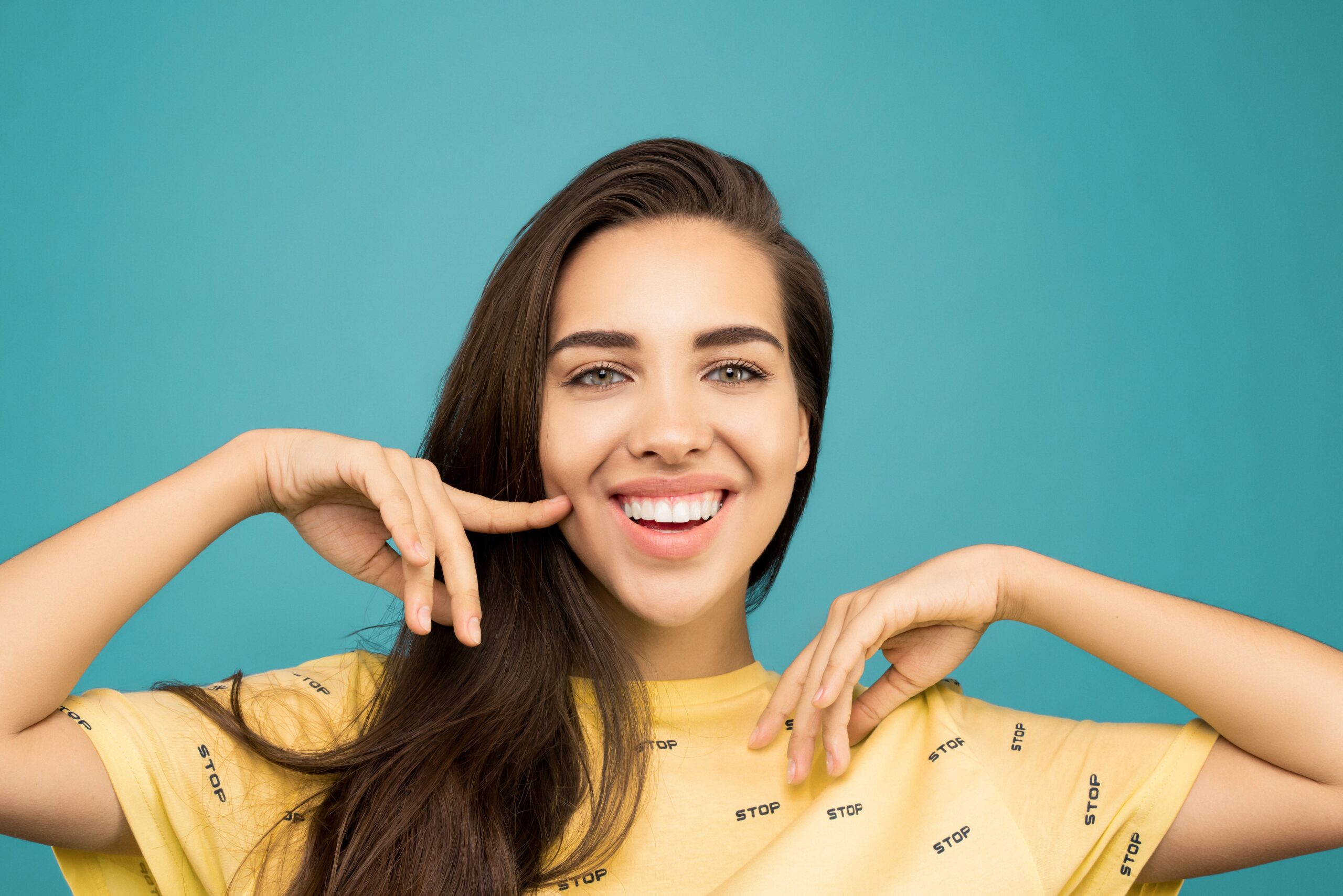A woman smiling while pointing to her white teeth
